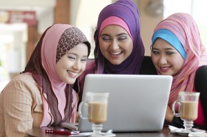 young muslim woman in head scarf using laptop in cafe with friends
